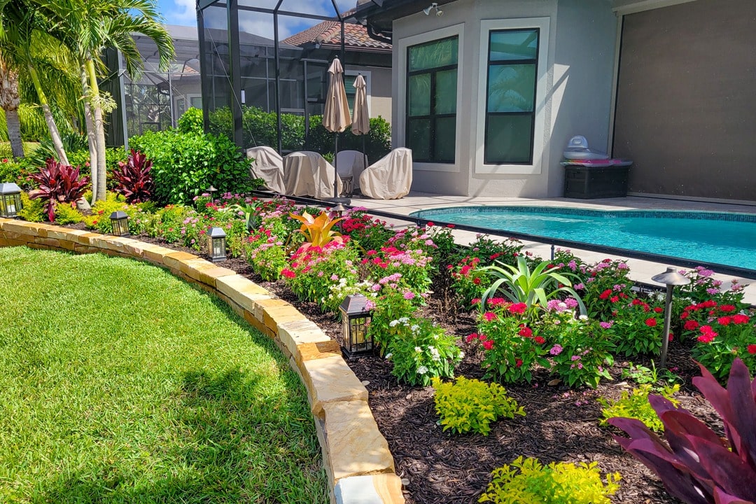 A backyard garden with colorful flowers, stone border, and small lanterns.
